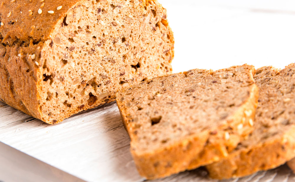 Das fertige Dinkelbrot mit getrockneten Tomaten, Oliven und Thymian auf einem Brettchen serviert